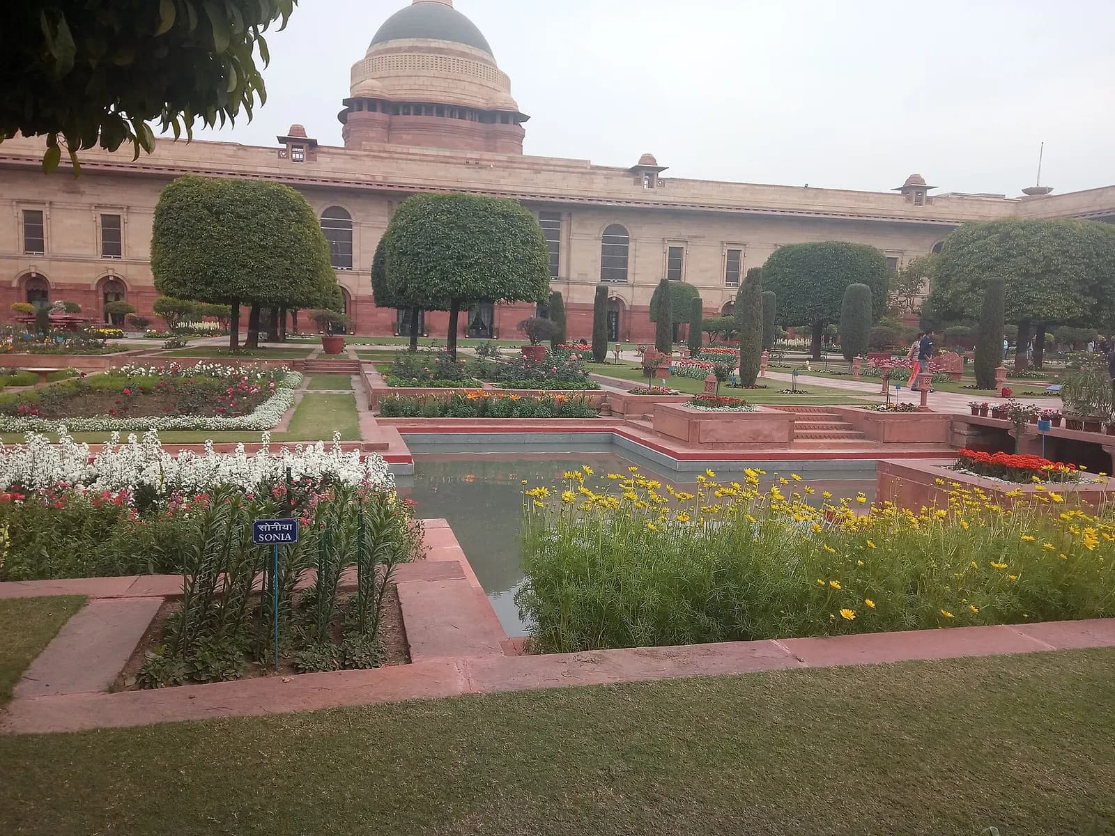 Formal garden with paved walkways and clipped hedges in front of a large sandstone building